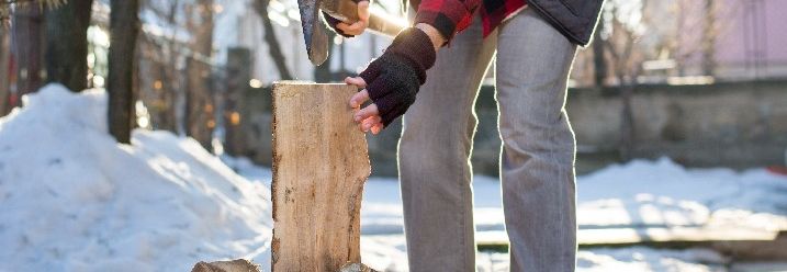 Ein Mann im winterlichen Garten setzt Axt zum Holz hacken an.